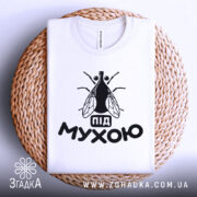 Футболка під мухою білого кольору, складена на плетеній основі, фон світлий, принт чорного кольору з малюнком мухи та написом 'під мухою'.