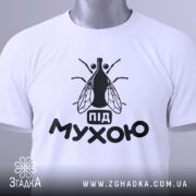 Футболка під мухою білого кольору, зображена зверху, на ній видно чорний принт з малюнком мухи та написом 'під мухою', на комірці є етикетка.