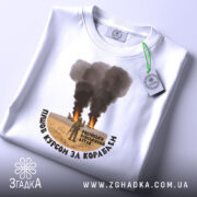 Футболка пішов курсом. Біла футболка, складена на столі, з принтом, що зображує військову сцену. Принт розташований по центру, текст чорного кольору обрамляє зображення. На футболці є етикетка з зеленим шнурком.