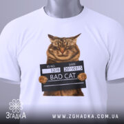 Футболка поганий кіт арешт, біла, зображена зверху, на фоні світлого градієнта, принт з котом у поліцейській табличці з написом 'BAD CAT', з зеленим ярликом.