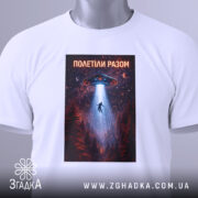 Футболка полетіли разом, білого кольору, складена на поверхні, фон світло-сірий, принт з космічним кораблем, що світить на людину, оточену лісом, з етикеткою на зеленому шнурку.
