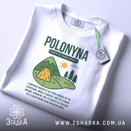Футболка полонина карпати, біла, розкладена на поверхні, з видимою етикеткою, фон світлий, принт з малюнком гір, сонця та текстом про полонину.