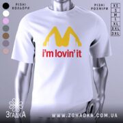 Футболка поп арт іронія, біла, зображена на манекені з правого боку, фон світло-сірий, принт жовтого кольору у формі літери М з червоним написом 'i'm lovin' it'.