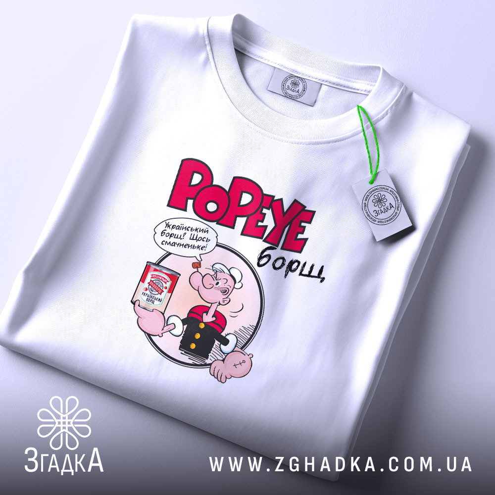 Футболка Popeye борщ, біла, складена на поверхні, фон світло-сірий, принт з Попаєм, який тримає банку борщу, текст червоним кольором, на комірці є етикетка.