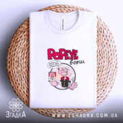 Футболка Popeye борщ, біла, складена на плетеній кошику, фон світлий, принт з Попаєм, який тримає банку борщу, текст червоним кольором.