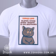 Футболка порада дня: Біла футболка з принтом кота, зображена зверху, фон світлий, на футболці видно текст поради дня, а також тег з логотипом бренду.