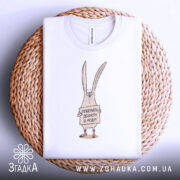 Футболка поверніть доброту, біла, складена на плетеній кошику, фон світлий, принт з малюнком кролика, що тримає табличку з написом 'Поверніть доброту в моду!'.