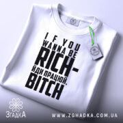 Футболка працюй будь багатим. Біла футболка, складена на поверхні, з чорним принтом. Вид зверху, фон світлий. Принт містить текст: 'IF YOU WANNA BE RICH- йди працею, BITCH', з етикеткою, що звисає з коміра.