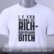Футболка працюй будь багатим. Біла футболка, складена на поверхні, з чорним принтом. Вид зверху, фон світлий. Принт містить текст: 'IF YOU WANNA BE RICH- йди працею, BITCH', з етикеткою, що звисає з коміра.