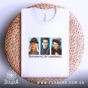 Футболка прекрасні бо українки. Біла футболка, зображена на плетеній основі, три персонажі в кольорових костюмах на грудях, текст "Прекрасні, бо українки!" під ними, фон натуральний, з елементами текстури.