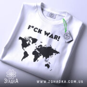 Футболка проти війни, складена біла футболка з чорним принтом у вигляді карти світу та написом 'F*CK WAR!', на етикетці зелена стрічка, фон світло-сірий.