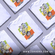 Футболка пригоди хлопців, біла, зображена на манекені, фон нейтральний, принт з чотирма персонажами на кольорових прямокутниках: зелений, жовтий, оранжевий, червоний.