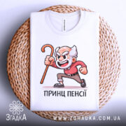 Футболка Принц Пенсії білого кольору, зображена зверху на плетеній кошику, фон світло-сірий, принт з дідусем у червоній сорочці, який тримає палицю, виглядає стильно.