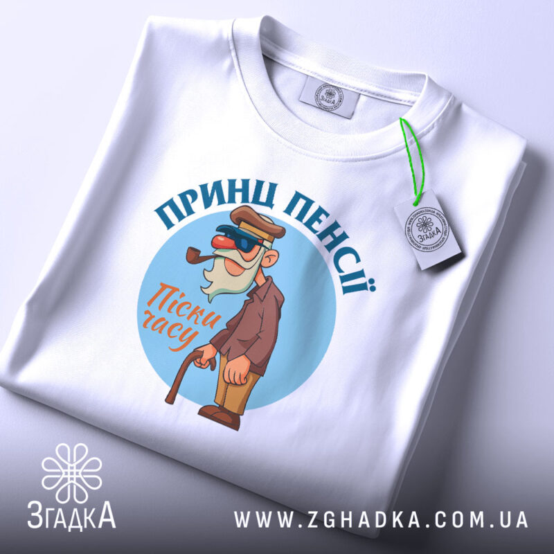 Футболка принц пенсії, білого кольору, складена на столі, фон світло-сірий, принт з мультяшним персонажем у капелюсі та окулярах, тримає тростину, текст 'Пісні часу' під персонажем, на футболці прикріплена етикетка.