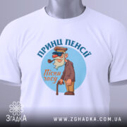 Футболка принц пенсії, білого кольору, складена на столі, фон світло-сірий, принт з мультяшним персонажем у капелюсі та окулярах, тримає тростину, текст 'Пісні часу' під персонажем, на футболці прикріплена етикетка.