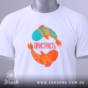 Футболка пристрасть риби. Складена біла футболка з принтом двох рибок, одна блакитна, інша оранжева. На футболці напис 'ПРИСТРАСТЬ'. Вид зверху, фон світло-сірий, з етикеткою на футболці.