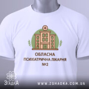 Футболка психіатрична лікарня, біла, складена на столі, фон світло-сірий, принт з будівлею лікарні в зеленому колі, текст під принтом: 'ОБЛАСНА ПСИХІАТРИЧНА ЛІКАРНЯ №2', на комірці видно етикетку.