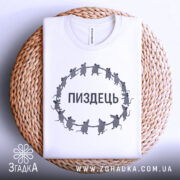 Футболка пиздець, біла, складена на плетеній кошику, фон світло-сірий, принт з мишами, що тримаються за руки, текст "ПИЗДЕЦЬ" великими літерами.