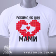 Футболка робимо як для мами, біла, зображена зверху на плоскій поверхні, фон світло-сірий, принт червоного кольору у формі серця з контуром України, напис чорним шрифтом, на комірці є етикетка.