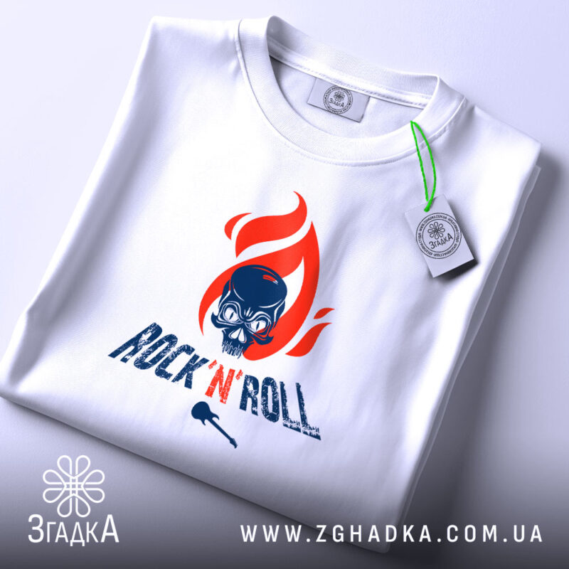 Футболка Rock N Roll білого кольору, зображена з верхнього ракурсу, на ній видно етикетку з зеленим шнурком, фон світло-сірий, принт з червоним полум'ям та черепом, текст 'ROCK'N'ROLL' у темно-синьому кольорі.