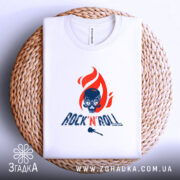 Футболка Rock N Roll білого кольору, зображена зверху на плетеній кошику, фон світло-сірий, принт з червоним полум'ям та черепом, текст 'ROCK'N'ROLL' у темно-синьому кольорі.