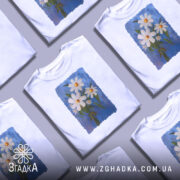 Футболка ромашки, білого кольору, зображена з фронтального ракурсу на манекені, фон світло-сірий, принт з трьох ромашок на блакитному фоні з зеленим листям.