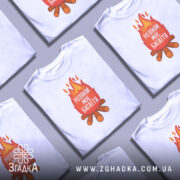 Футболка розпали моє багаття, біла, зображена з переднього ракурсу на манекені, фон світлий, принт з вогнем та текстом "РОЗПАЛИ МОЄ БАГАТТЯ" на червоному фоні, під ним зображення дров.