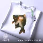 Футболка рибак на заході, складена біла футболка на світлому фоні, принт з рибою та рибалкою, етикетка з зеленим шнурком.