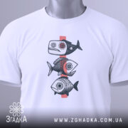 Футболка рибний етно, біла, зображена зверху на плоскій поверхні, фон світло-сірий, принт з трьох риб у стилі етно, з етикеткою зеленого кольору.