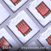 Футболка сардини білого кольору, зображена на манекені, з принтом у вигляді консервної банки з сардинами, червоний текст на зеленому фоні, фон світло-сірий.