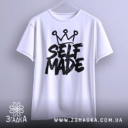 Футболка self made білого кольору, підвішена на вішалці, фон світло-сірий, принт чорного кольору з написом 'SELF MADE' та короною зверху, вид спереду.