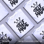 Футболка self made білого кольору, зображена з правого ракурсу на манекені, фон світло-сірий, принт чорного кольору з написом 'SELF MADE' та короною зверху.