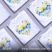 Футболка серце карпатський мотив, біла, зображена на манекені, фон світло-сірий, принт містить жовте сонце, сині гори та різнокольорові рослинні елементи.