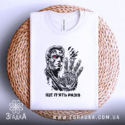 Футболка ще п’ять разів. Біла футболка, складена на плетеній кошику, фон світлий, принт з персонажем на грудях, деталі принта добре видно, з червоним оком та механічною рукою.