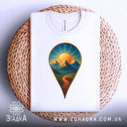 Футболка шлях до пригод. Біла футболка з принтом у вигляді геолокаційної позначки, на якій зображені гори та сонце, складена на плетеній кошику з нейтральним фоном. Принт чіткий і кольоровий.