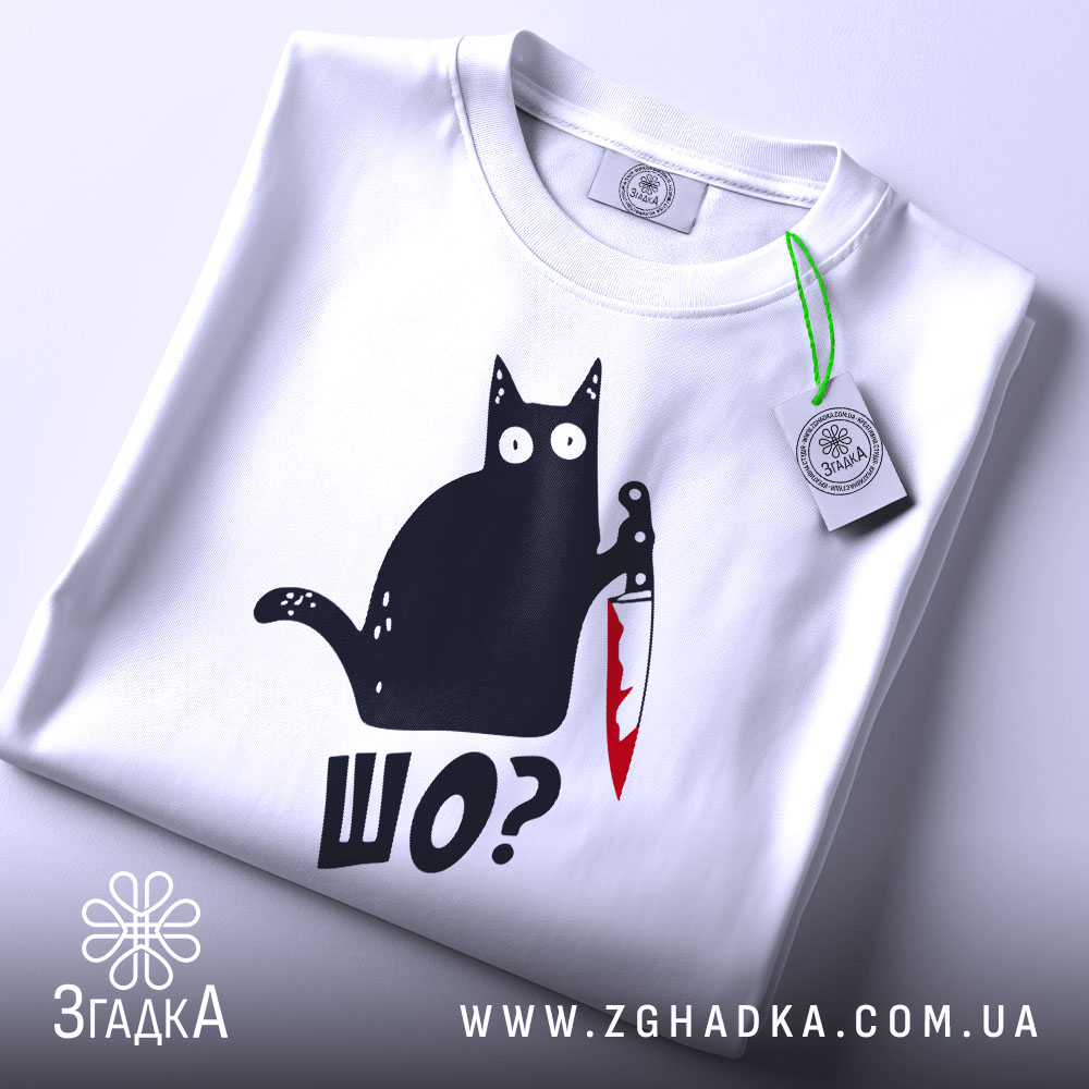Футболка шо чорний кіт білого кольору, зображена зверху, на ній видно етикетку з зеленим шнурком, фон світло-сірий, принт з чорним котом, що тримає ніж з червоною лезом, текст 'ШО?' під котом.