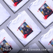 Футболка шукай свій шлях. Біла футболка на манекені, з принтом на грудях, що зображає жінку в темних окулярах та хустці, на фоні жовто-блакитного прапора. Принт доповнений червоними плямами, що нагадують кров, та написом українською мовою.