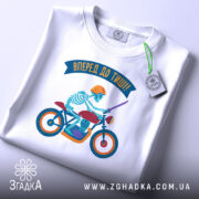 Футболка скелет на мотоциклі, біла, зображена з верхнього ракурсу, фон світло-сірий, принт з скелетом у шоломі на червоному мотоциклі, з зеленим ярликом та написом 'Вперед до тиші!'.