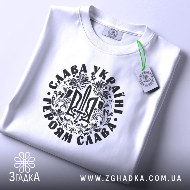 Футболка Слава Україні, білого кольору, складена на поверхні, фон світло-сірий, принт чорного кольору з тризубом та написом 'Слава Україні! Героям Слава!', на футболці є етикетка з зеленим шнурком.