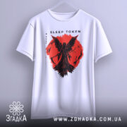 Футболка Sleep Token білого кольору, підвішена на вішалці, з принтом червоного кольору, що зображає фігуру з крилами на фоні червоного кола, фон світло-сірий, видно деталі принта.