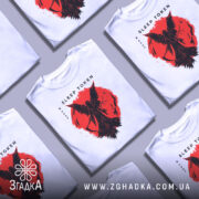 Футболка Sleep Token білого кольору, зображена на манекені, з принтом червоного кольору, що зображає фігуру з крилами на фоні червоного кола, фон світло-сірий, видно деталі принта.