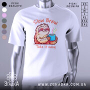 Футболка Slow Brew релакс білого кольору, зображена з фронтального ракурсу на манекені, фон нейтральний, принт з ведмедем-лінивцем, який тримає чашку з парою, текст 'Slow Brew' і 'Take it easy' виконаний у яскравих кольорах.