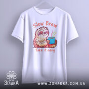 Футболка Slow Brew релакс білого кольору, зображена з фронтального ракурсу на вішалці, фон світлий, принт з ведмедем-лінивцем, який тримає чашку з парою, текст 'Slow Brew' і 'Take it easy' яскраво оформлений.