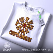Футболка смерть зачекає, біла, зображена зверху, на фоні світло-сірого градієнту, принт з символом та написом 'СМЕРТЬ ЗАЧЕКАЄСЬ' виконаний в золотистих та червоних кольорах, з зеленим ярликом.