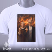 Футболка сміливий політичний принт, біла, зображена на столі, фон світлий, принт з двома персонажами, які показують середні пальці, прикріплена бірка з зеленим шнурком.