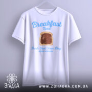 Футболка сніданок новий день, біла, підвішена на вішалці, фон світло-сірий, принт з написом 'Breakfast Time' та зображенням хліба з шоколадом.