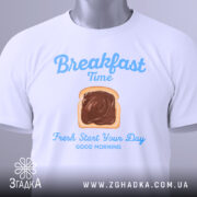 Футболка сніданок новий день, біла, складена на поверхні, фон світло-сірий, принт з написом 'Breakfast Time' та зображенням хліба з шоколадом, з етикеткою.