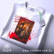 Футболка сьогодні хороший день. Біла футболка, розкладена на поверхні, з видимим етикеткою. Принт на футболці той же, що й на попередній, з червоними плямами та текстом. Фон нейтральний, що підкреслює дизайн футболки.