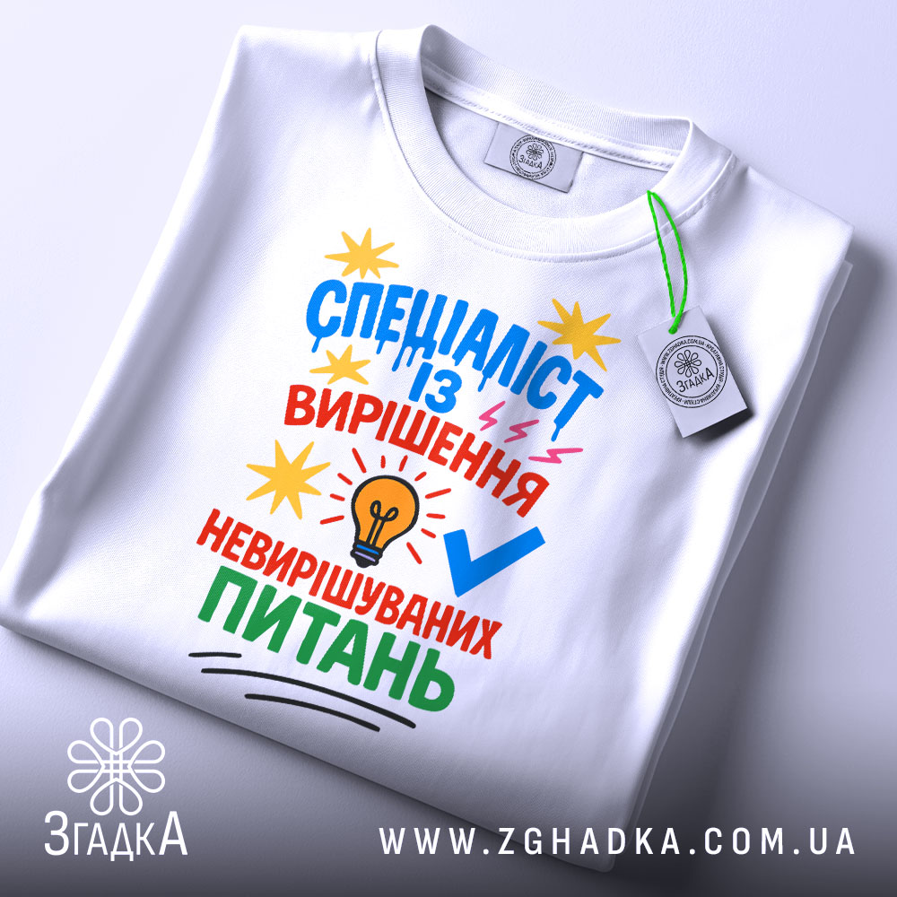 Футболка спеціаліст із питань білого кольору, зображена зверху, на плоскій поверхні, фон світло-сірий, принт яскравий з текстом та графічними елементами, на комірці видно етикетку.