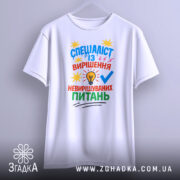 Футболка спеціаліст із питань білого кольору, зображена з фронтального ракурсу на вішалці, фон світло-сірий, принт яскравий, текст та зображення лампочки, зірочок і галочки.